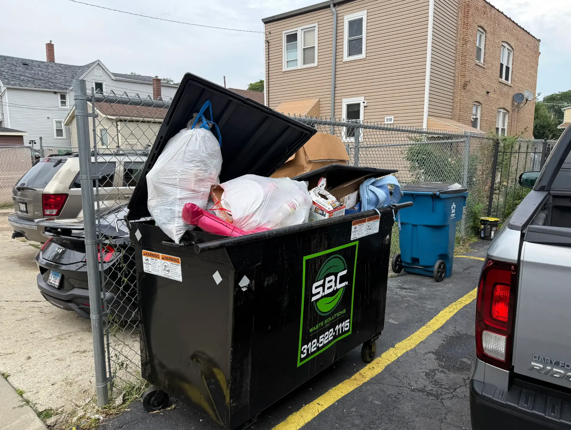 Overflowing dumpster packed with bags and boxes behind a Chicago building.