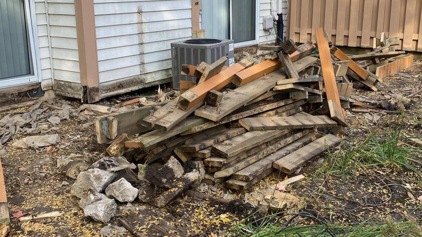 Old deck boards lay in a pile behind a home and are ready to be disposed of.