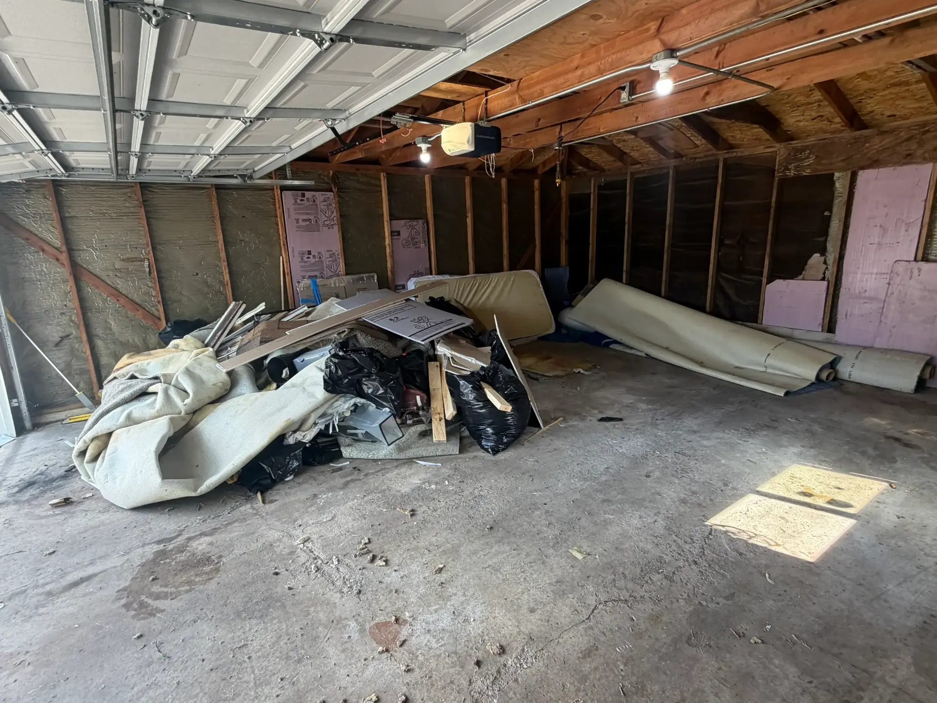 Garage filled with construction debris, carpet, drywall and trash bags before removal