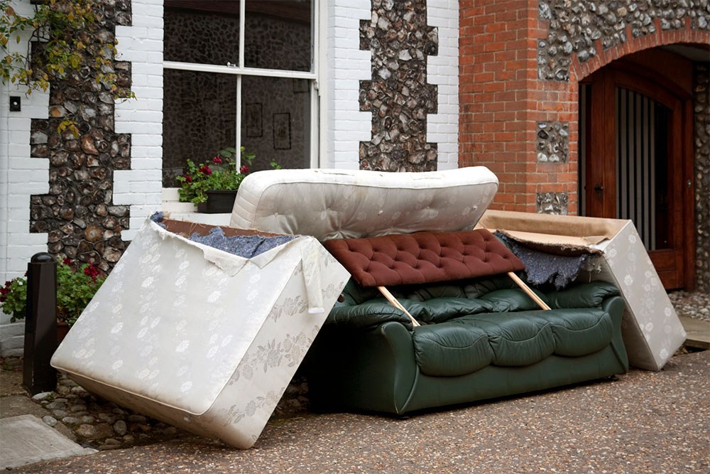 I pile of mattresses and couches sits outside of a building.