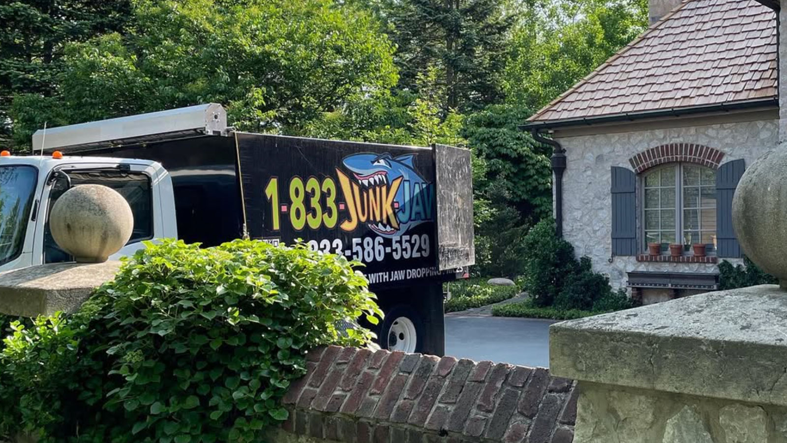 A Junk Jaws truck is parked in front of a large estate ready to load with unwanted junk.