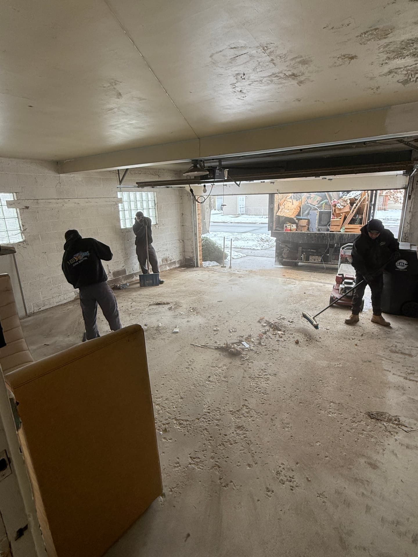 The Junk Jaws crew sweeping out a garage with the truck loaded in the driveway.