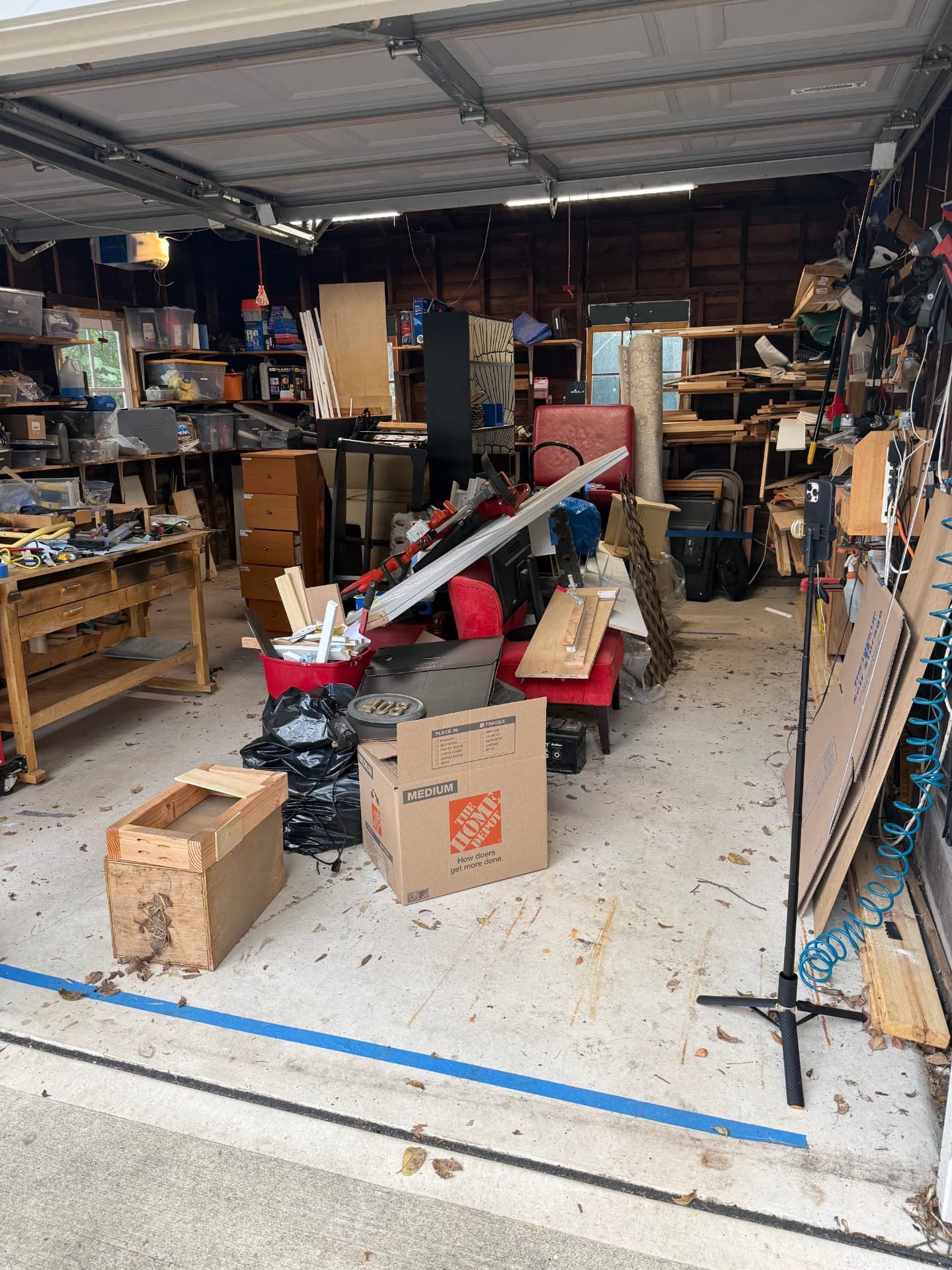 A garage workshop filled with lumber, tools and old furniture waiting to be hauled away.