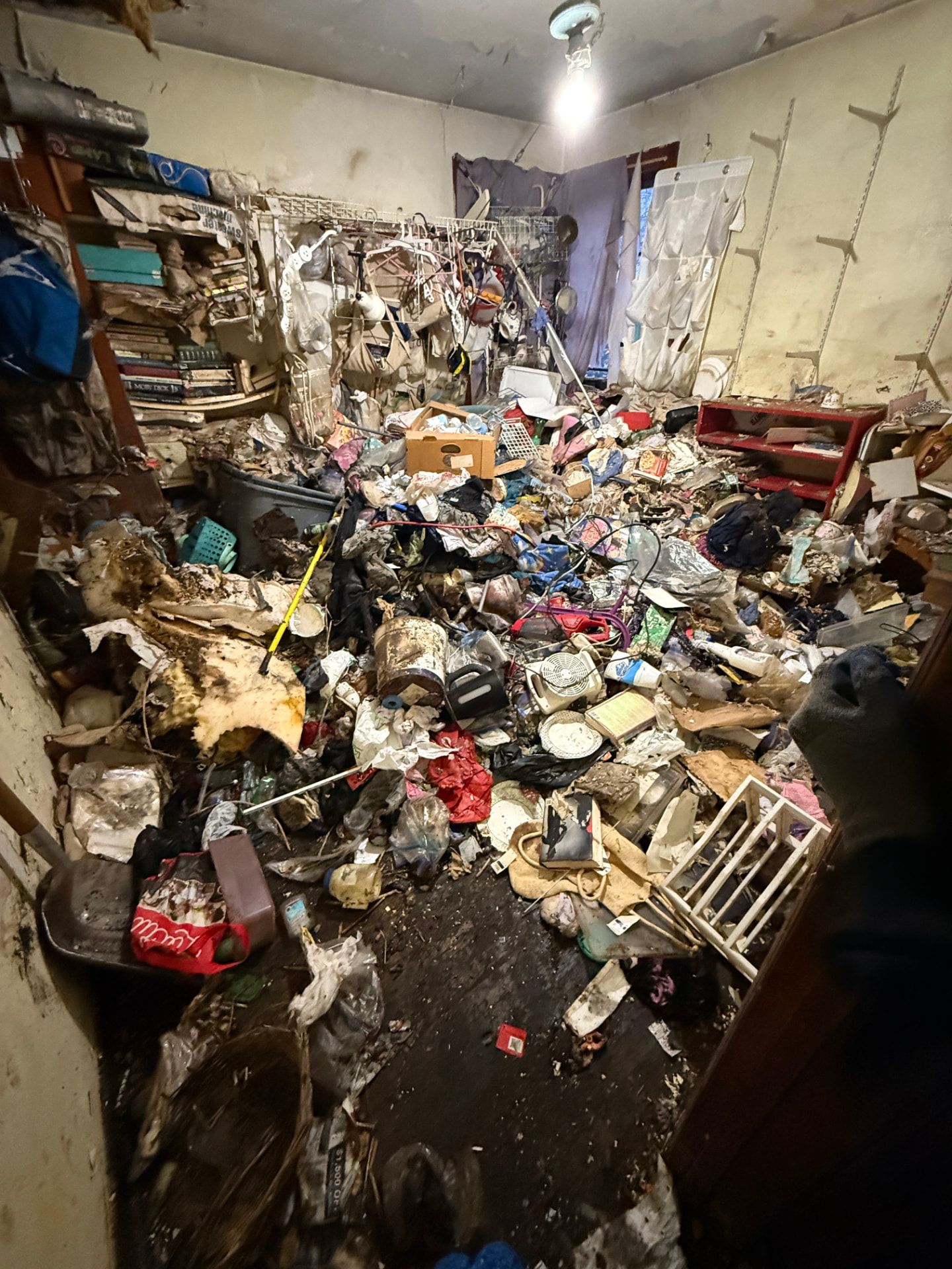 A back room buried in debris requiring protective gear during a hoarding cleanout.
