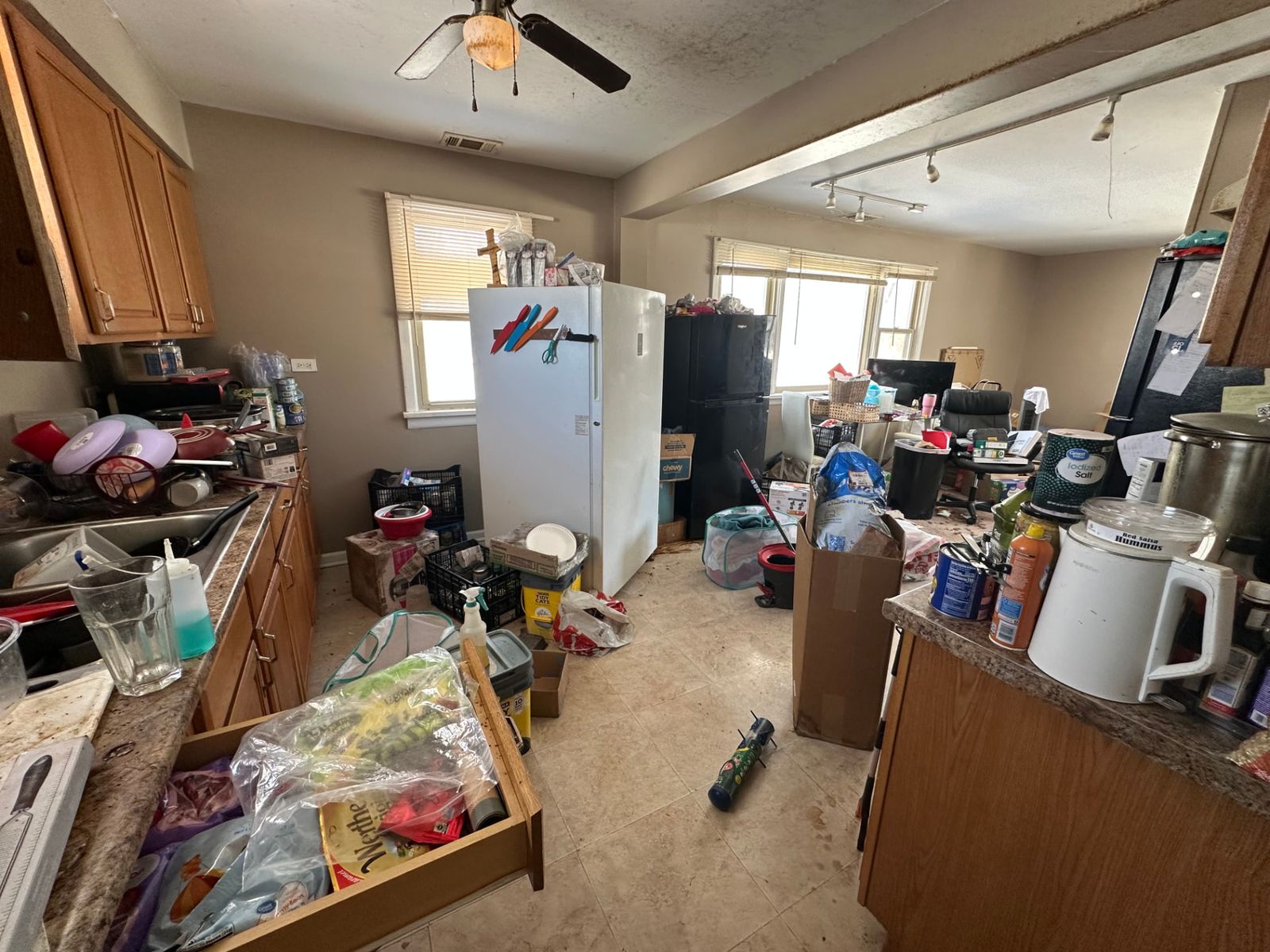 A cluttered kitchen filled with boxes, bags and household items before disposal and sorting.