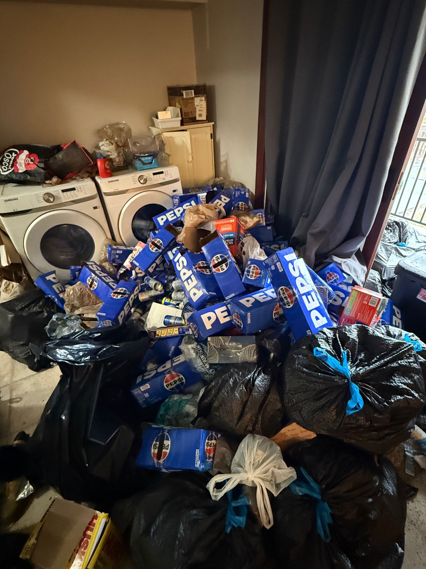 Stacks of soda boxes and trash bags piled around a laundry area during a hoarding cleanout.