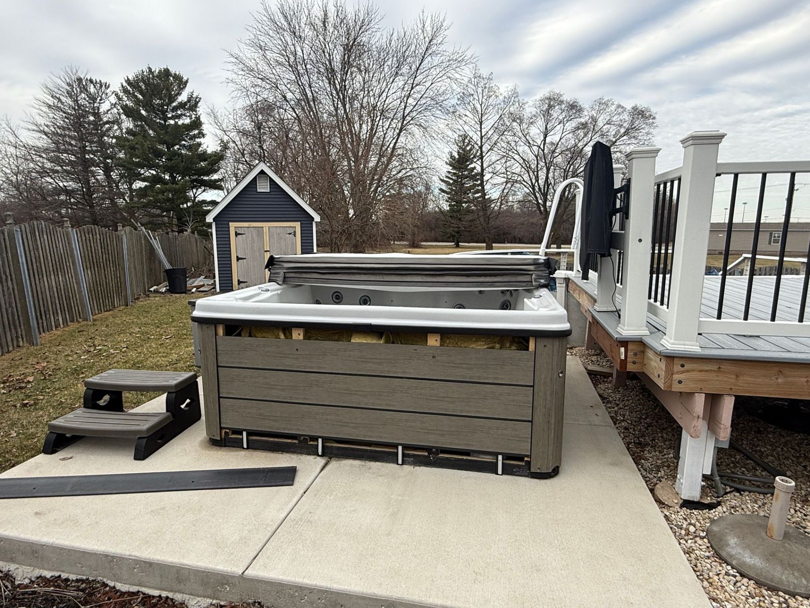 A large backyard hot tub on a concrete pad next to a deck, ready for removal.