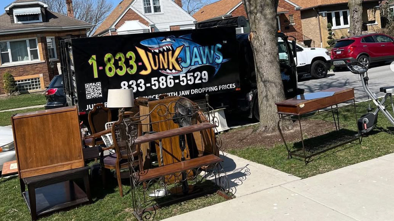 Joe from Junk Jaws stands in the bed of a truck next to a pile of office furniture he has loaded for disposal.