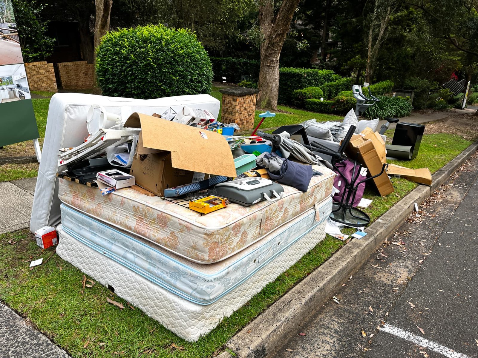 Mattress, box spring, and household items stacked at the curb for mattress removal pickup.