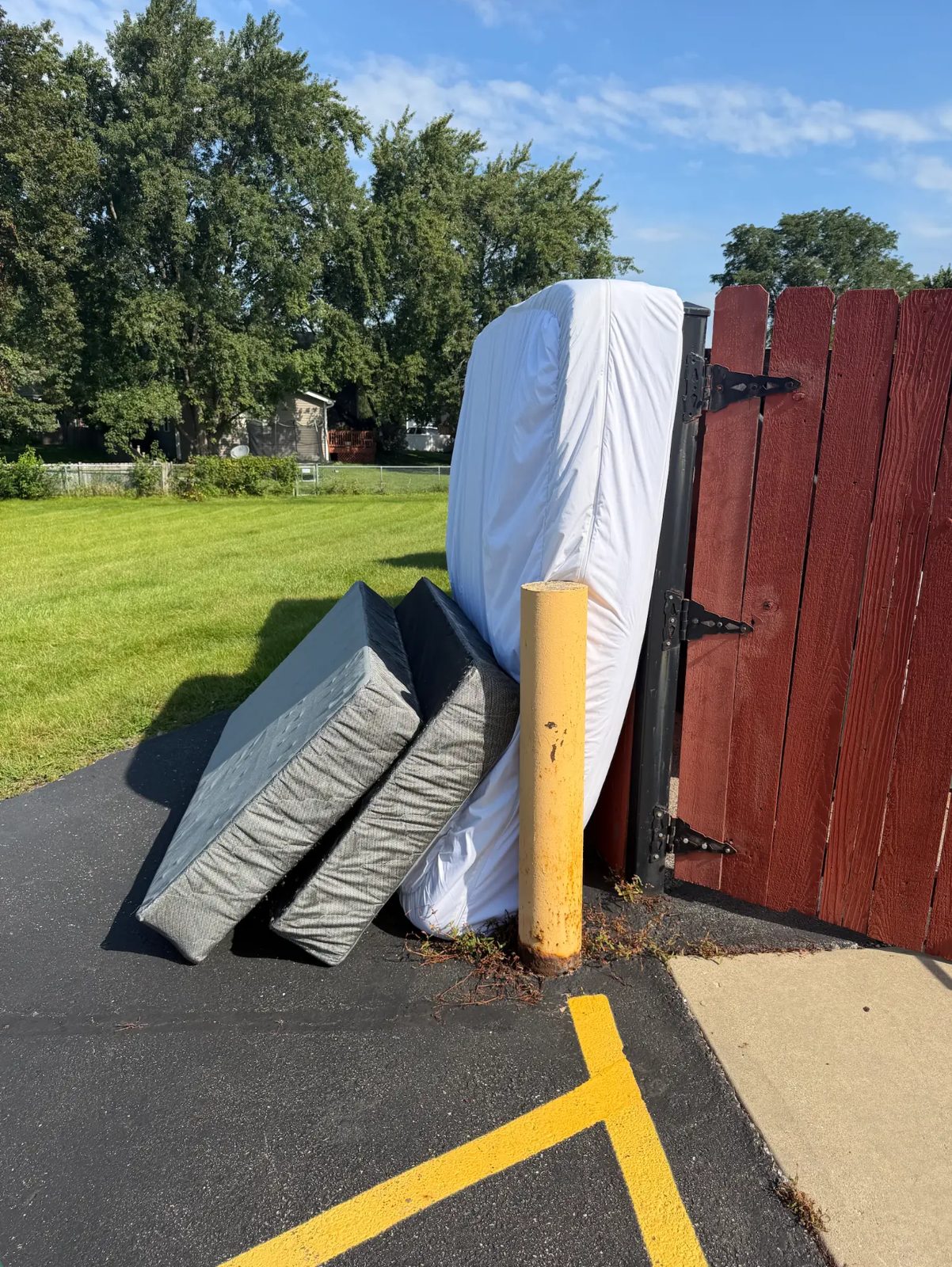Mattress and two box springs set out by a fence gate for Junk Jaws mattress pickup.