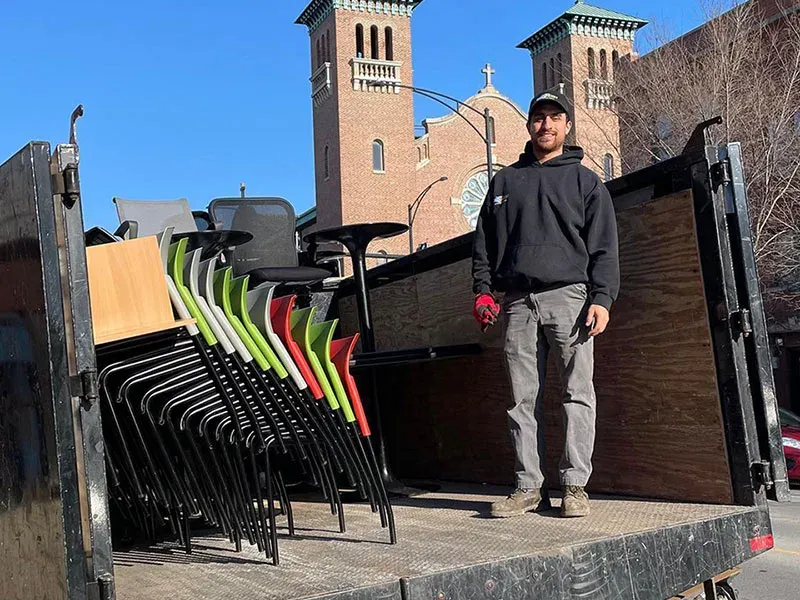 A Junk Jaws crew member on the truck bed with stacked office chairs, desks, and a conference table.