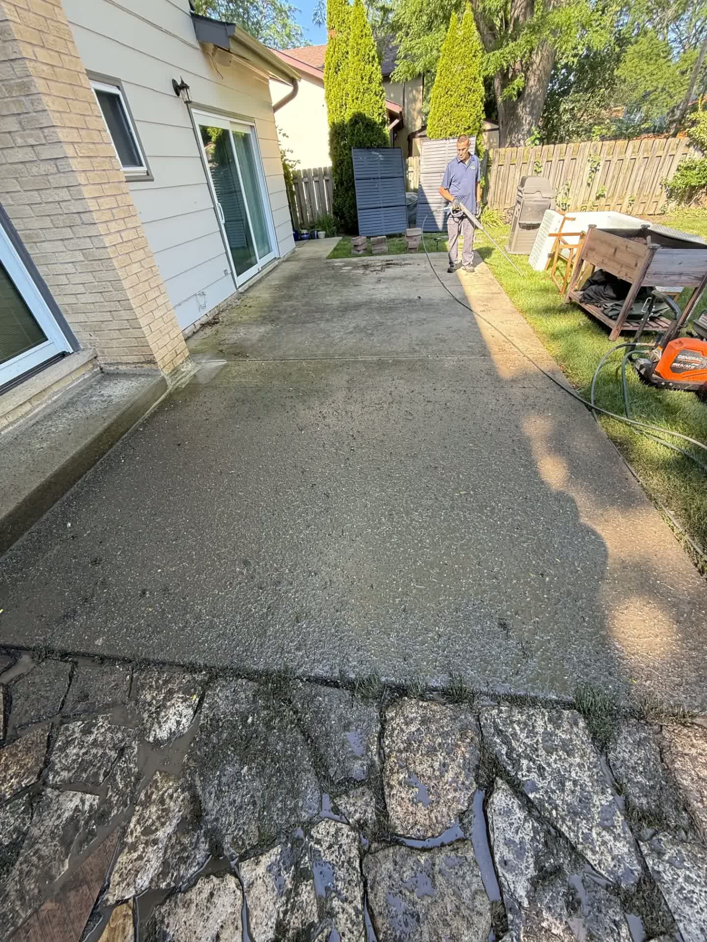A dirty concrete patio being pressure washed by a Junk Jaws technician.