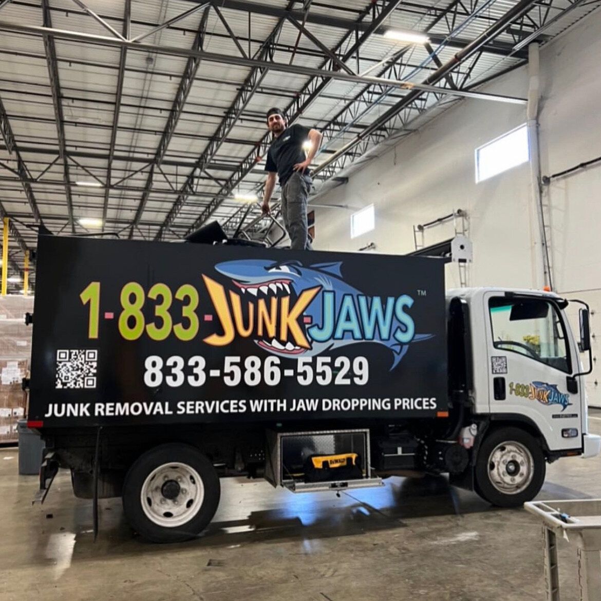 A Junk Jaws crew member standing on the truck bed inside a warehouse.